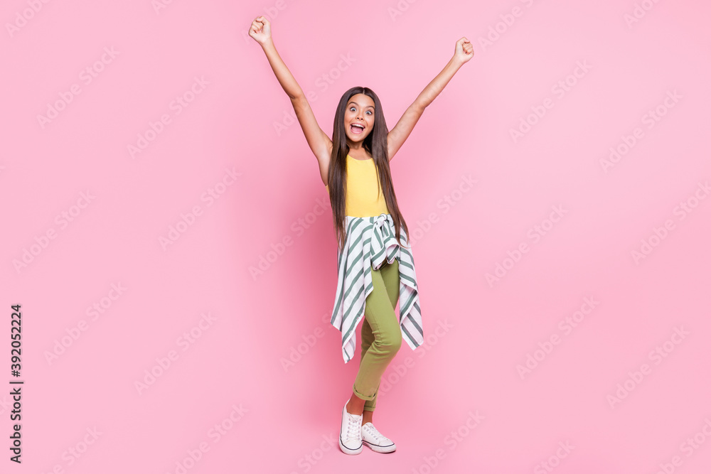 Full size photo of happy little brown haired girl raise fists wear green pants yellow singlet isolated on shine pink color background