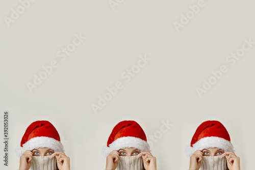 Close up the concept of three young beautiful women over isolated beige background Santa hats, looking at the camera covering his face with a collar © BARLIAEVA