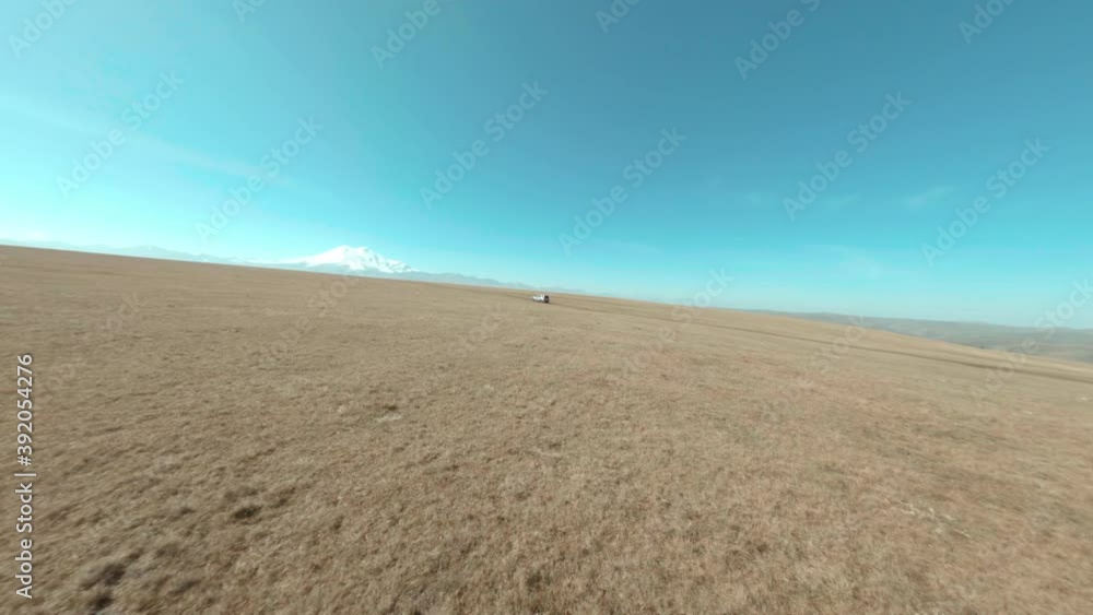 Fpv sport drone shooting car driving on off-road field in hilly terrain on background snowy Elbrus mountain. SUV automobile action extreme travel through Kabardino Balkaria region. Fpv sport drone shooting car driving on off-road field in hilly terrain on background snowy Elbrus mountain. SUV automobile action extreme travel through Kabardino Balkaria region.