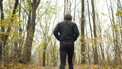 A young brutal Caucasian man is emotionally walking in an autumn park and listening to music on headphones. Dancing and relaxation