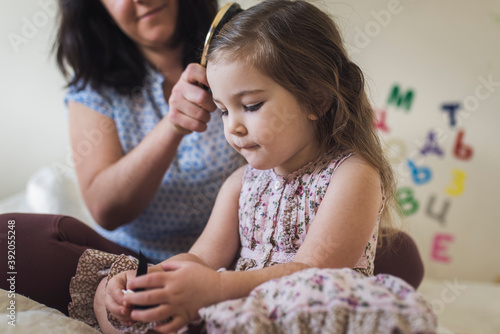 Mom brushing hair of 4 yr old daughter while sitting on bed photo