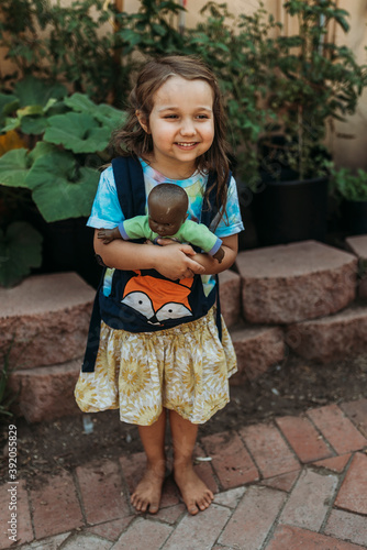 Preschool aged girl carrying babydoll in baby carrier outside in garde photo