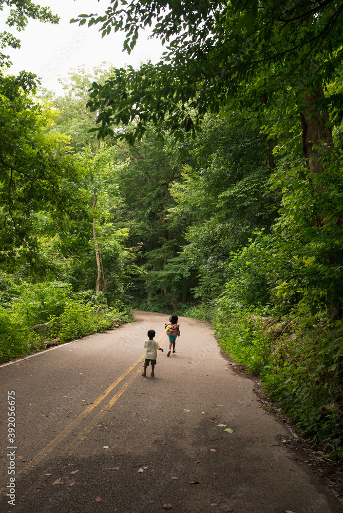 Kids running down a road with trees on both sides Kids running down a road with trees on both sides