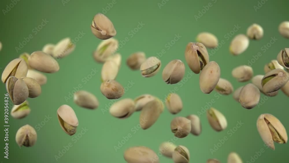 Close-up of salted pistachios flying up on a green background in slow motion Close-up of salted pistachios flying up on a green background in slow motion
