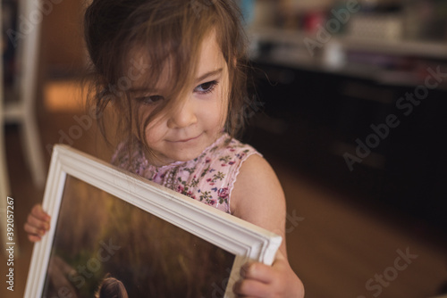 Sweet brown-eyed 4 yr old girl with wispy hair holding framed picture photo