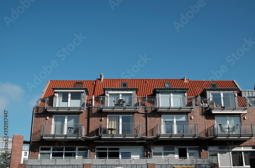 Mehrfamilienhaus mit Klinkerfassade, Balkons, Dachgauben und Ferienwohnungen vor blauen Himmel an der Küste der Nordsee in Bensersiel bei Esens in Ostfriesland in Niedersachsen photo