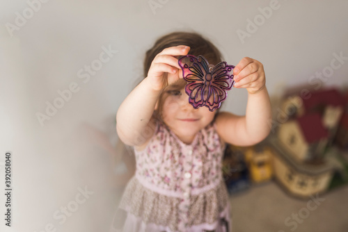 4 yr old girl in sleeveless dress examining butterfly suncatcher photo