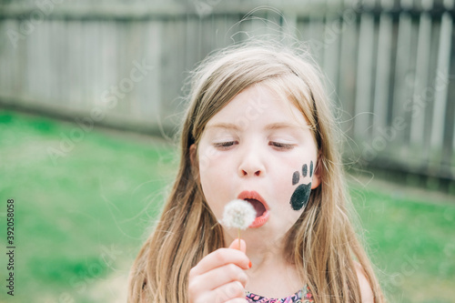 Young girl blowing a dandelion in the backyard photo