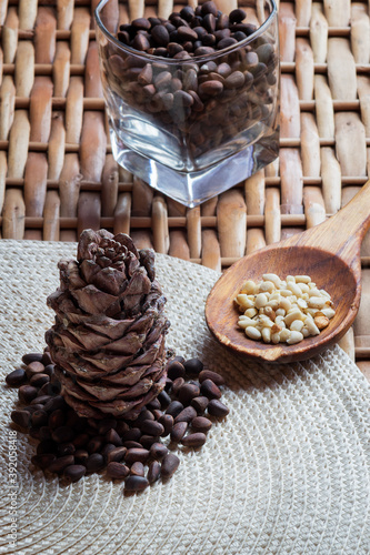 Cone, pine nuts in the glass and shelled nuts in the wooden spon on the braided surface. Vertical oriantation photo