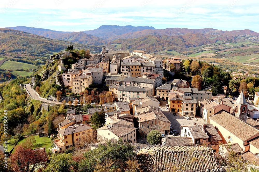 High angel view of beautiful small old town on the hill surrounded by mountains and colorful autumn trees against nice blue and clouds sky during autumn in Pennabilli,Province of Rimini,Italy