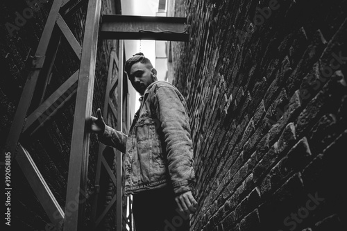 Young bearded man in a denim jacket walks through a brick alley