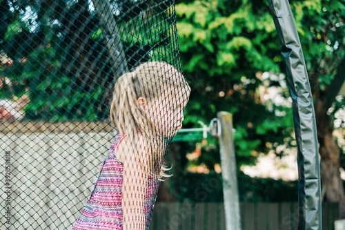 Young girl with grumpy face leaning on trampoline netting