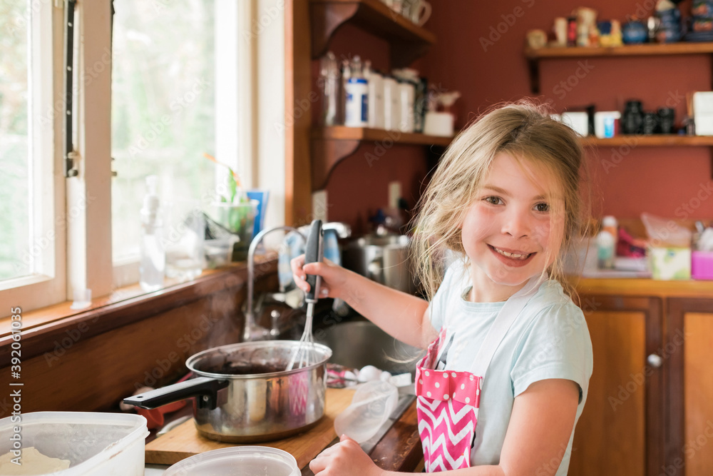 Young girl smiling and whisking hot baking mixture in messy kitchen Young girl smiling and whisking hot baking mixture in messy kitchen