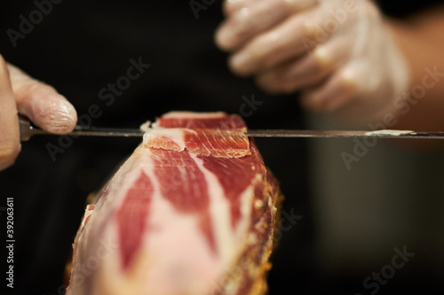 The chef is cutting the jamon. image of a ham cutter with a knife cutting a thin slice of ham. Dry Spanish ham, Jamon Serrano, Bellota, Italian Prosciutto Crudo or Parma ham.