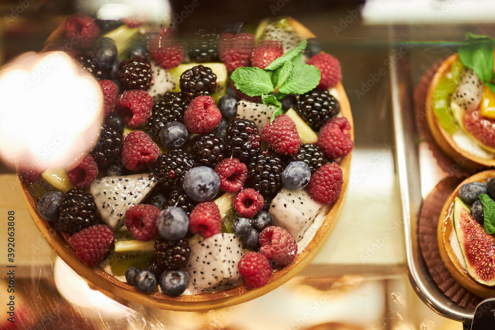 Cake with fresh berries on the glass counter in the bakery. cakes with fresh berries. tartlets with yogurt, raspberries and blackberries, strawberries and blueberries. Cake with fresh berries on the glass counter in the bakery. cakes with fresh berries. tartlets with yogurt, raspberries and blackberries, strawberries and blueberries.