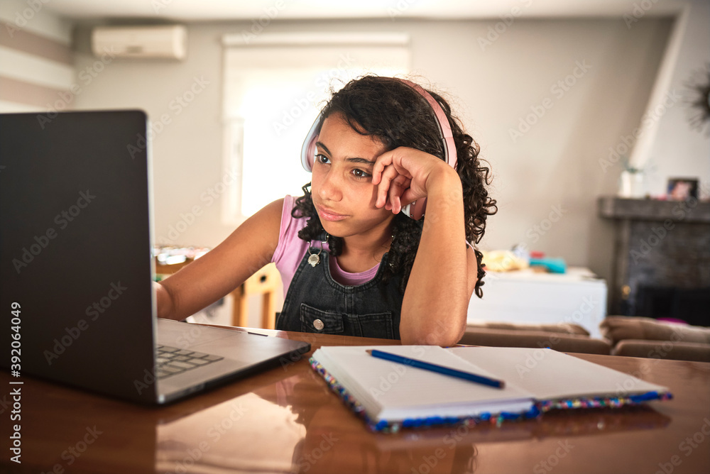 A bored girl doing her homework with her laptop at home A bored girl doing her homework with her laptop at home