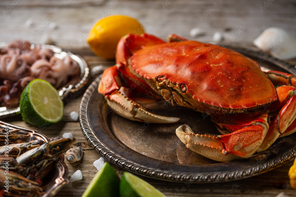 Close-up top view of cooked crab on baby octopuses and tiger shrimps background. Served with lime, lemon and seashells on rustic wooden table. Seafood concept. Delicious meal. Close-up top view of cooked crab on baby octopuses and tiger shrimps background. Served with lime, lemon and seashells on rustic wooden table. Seafood concept. Delicious meal.