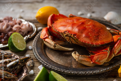 Close-up top view of cooked crab on baby octopuses and tiger shrimps background. Served with lime, lemon and seashells on rustic wooden table. Seafood concept. Delicious meal.