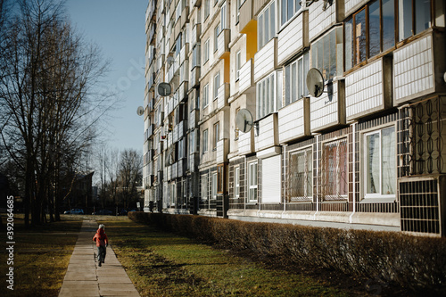 Back view of a boychild walking along a walkway having a residential building on a side photo