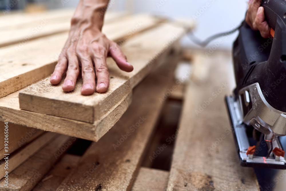 Hands of a young woman cutting wooden pallets with a jigsaw Hands of a young woman cutting wooden pallets with a jigsaw