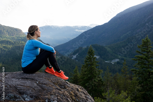 Strong sportswoman sitting and taking a break from trail running against forested mountain ridge during fitness workout in countryside photo