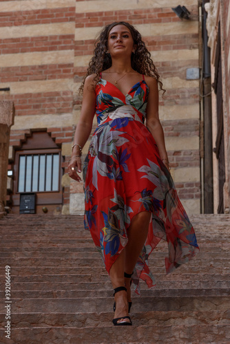 Young curly girl with colorful summer dress. Walks around the city by day, background of an ancient staircase.