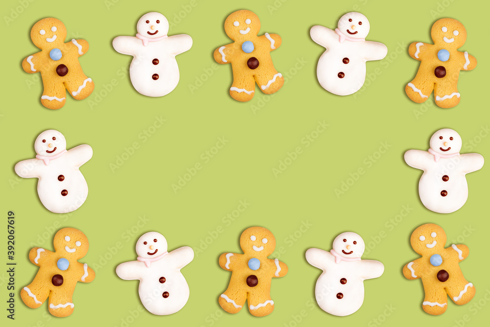 Christmas cookies frame in the shape of a snowman and a gingerbread man decorated with icing sugar and fondant on a green background
