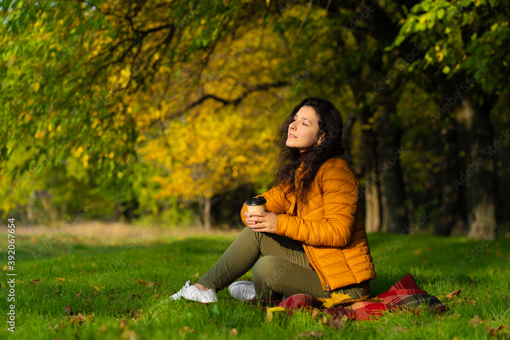Pretty girl enjoys autumn and the beauty of nature sitting on a green lawn in the park. Autumn mood Pretty girl enjoys autumn and the beauty of nature sitting on a green lawn in the park. Autumn mood
