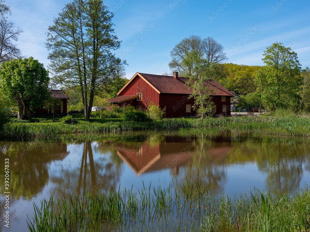 Red barn by a lake in Sweden. It is summertime and trees are reflecting in the water