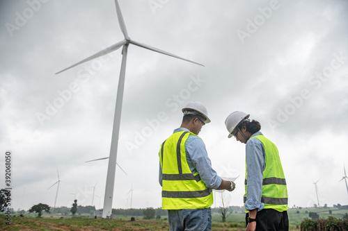 Two engineers working and holding the report at wind turbine farm Power Generator Station on mountain,Thailand people