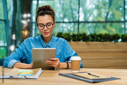 Nice-looking young caucasian businesswoman using tablet at the desk in modern office photo