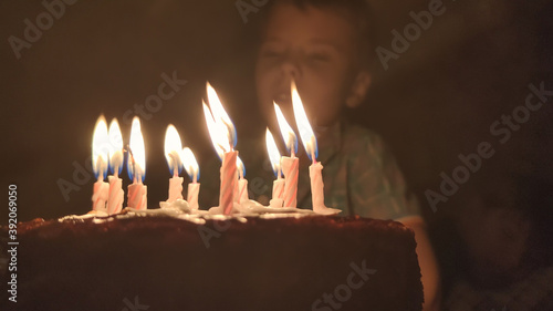 Cute boy blows out candles on a cake on his birthday. Happy child looks at a cake with candles. Happiness concept