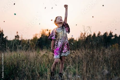 girl standing strong in a sparkly dress with star confetti falling