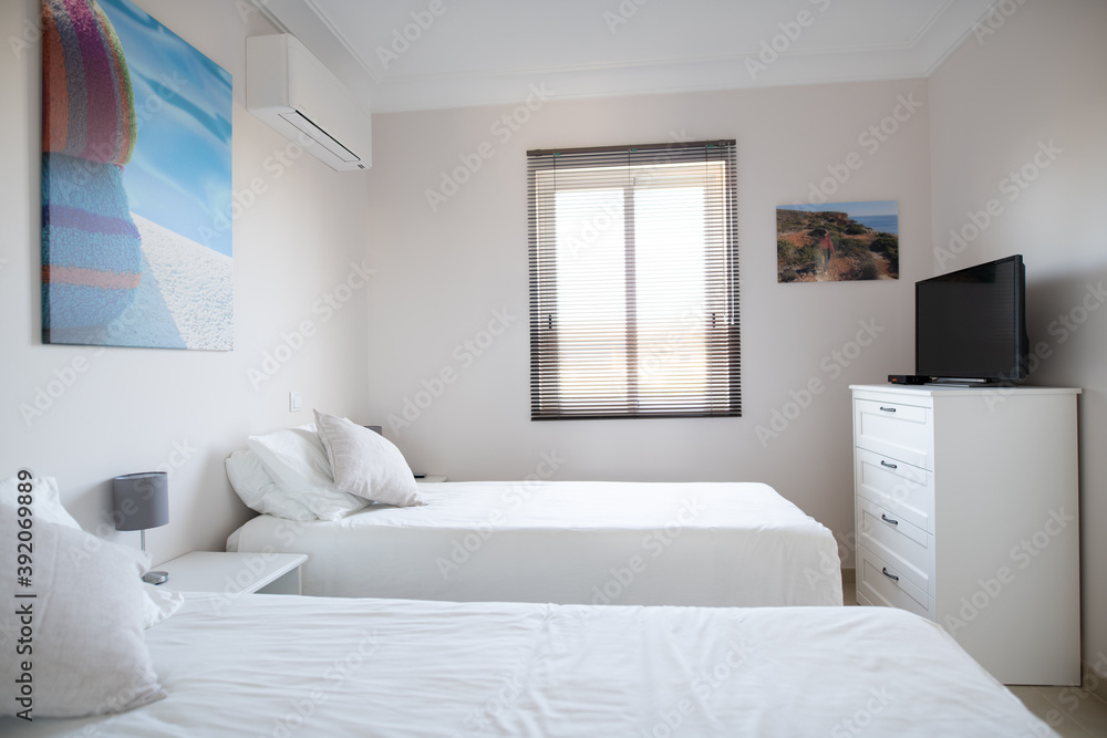 Clean twin bedroom in a house with white bed linen and white walls and cabinet with TV