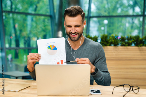 Confident smiling young businessman showing diagrams online using his laptop at office desk