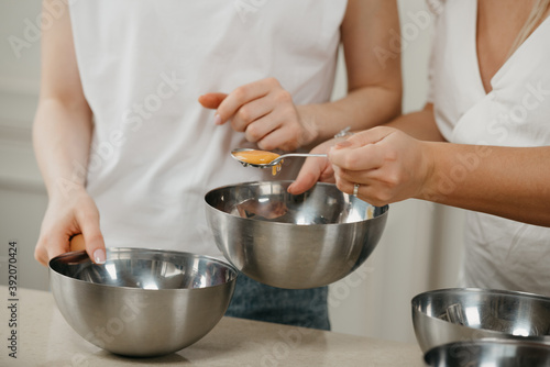 A close photo of the hands of two women, one of them is moving the yolk in a spoon to another stainless steel soup bowl in the kitchen.