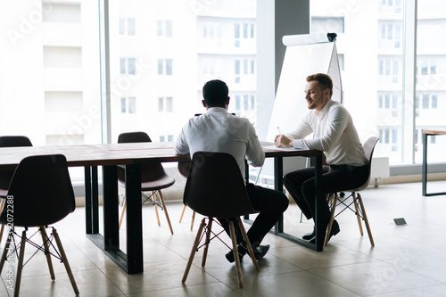 Caucasian businessman and African American business partner preparing the contract on paper document sitting at the office desk. Business people having informal business team meeting.