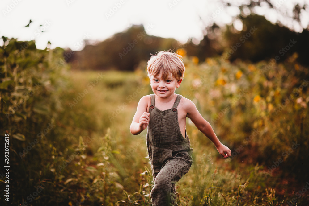 Smiling boy running in a field with sunflowers in the background Smiling boy running in a field with sunflowers in the background