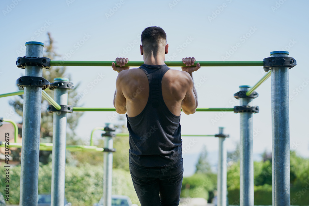 Back view of a man practicing calisthenics in a park on sunny day