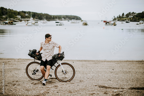 male cyclist takes break on beach in front of harbor, Harpswell, Maine photo