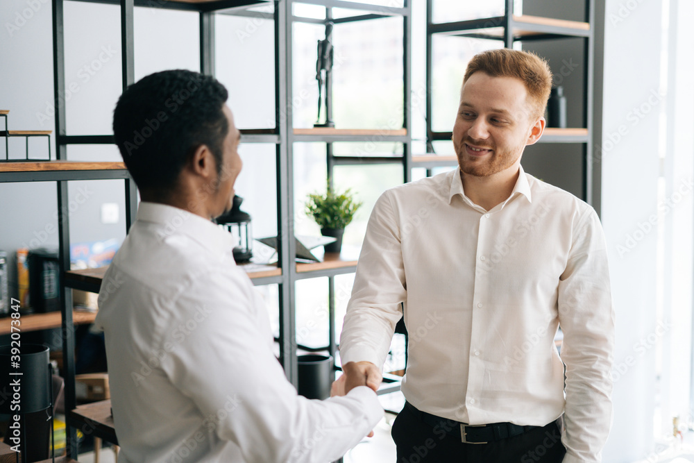Back view of two entrepreneurs shaking hands indoor in business office. African american and caucasian colleagues in modern office boardroom Back view of two entrepreneurs shaking hands indoor in business office. African american and caucasian colleagues in modern office boardroom