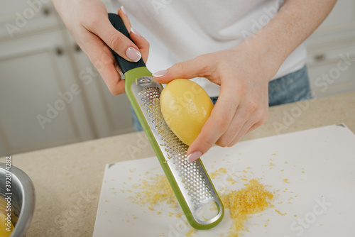 A close photo of the hands of a woman who is separating the lemon zest with a grater in the kitchen photo