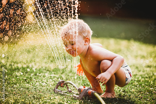White boy sticking tongue out drinking water from sprinkler in garden photo
