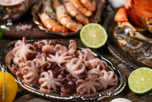 Close-up top view of assorted seafood. Cooked crab  baby octopuses and tiger shrimps served with lime and seashells on rustic wooden background. Seafood concept. Delicious meal.