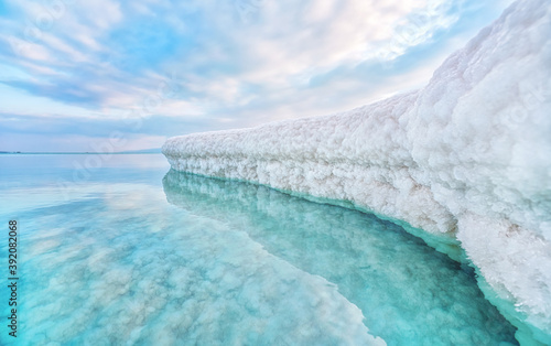 Sand completely covered with crystalline salt looks like ice or snow on shore of Dead Sea, turquoise blue water near, sky colored with morning sun distance - typical scenery at Ein Bokek beach, Israel photo