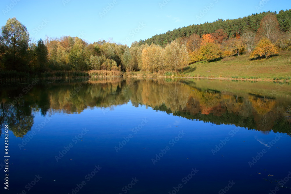 Blick auf den Gültlinger See. Der Herbstwald spiegelt sich im See.
