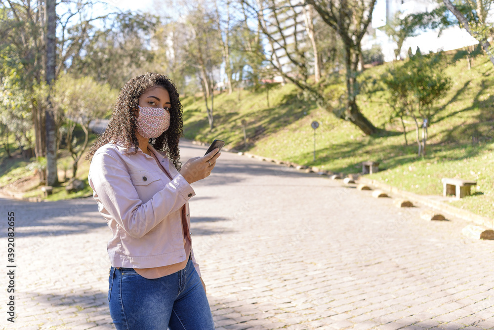 Black woman with facemask on urban background texting on cellphone Black woman with facemask on urban background texting on cellphone