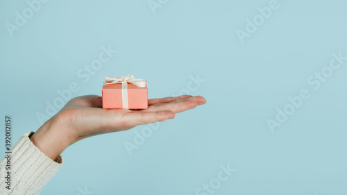 Giving Tuesday, Give, Help, Donation, Support, Volunteer concept with female hands and pink gift box on blue background. Heart shaped female fingers and pink gift box close up