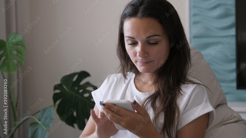 Happy young woman holding smart phone looking at cellphone screen enjoying using mobile apps for shopping having fun playing games chatting in social media sit on couch at home Happy young woman holding smart phone looking at cellphone screen enjoying using mobile apps for shopping having fun playing games chatting in social media sit on couch at home