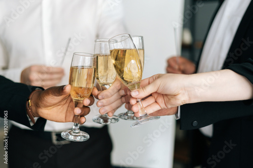 Close-up view of business team of multinational employees holding clinking glasses of champagne and smiling cheerfully at corporate New Year or Happy Christmas eve.